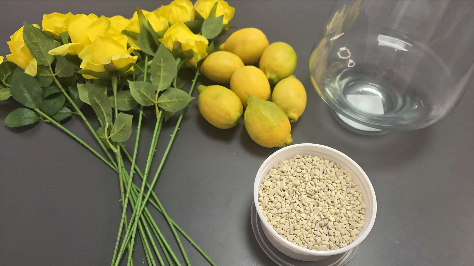Materiales necesarios para crear el centro de mesa: jarrón de cristal, piedra decorativa color crema 3/6 mm, limones naturales y rosas amarillas artificiales. Una combinación sencilla para conseguir una decoración fresca y veraniega.